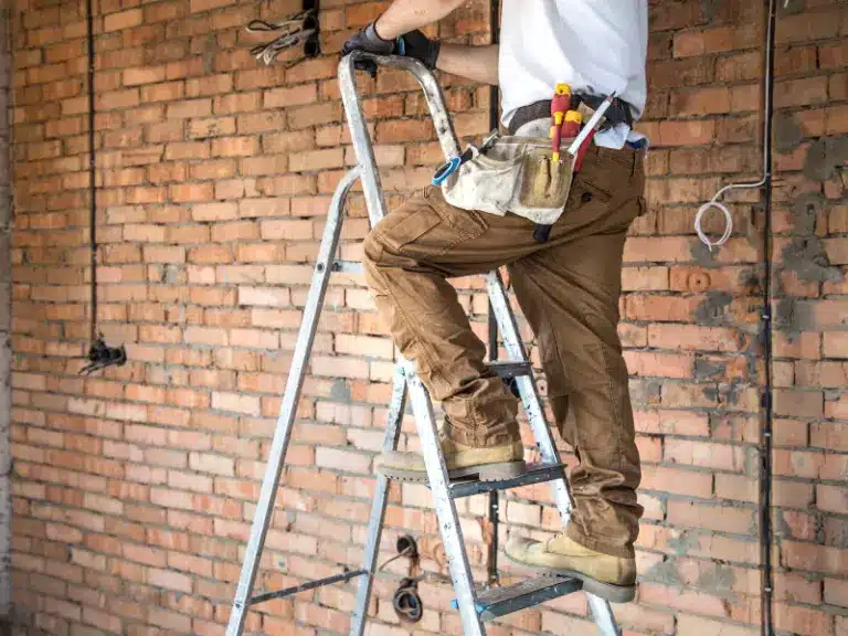 Mann in Arbeitsklamotten steigt auf Leiter